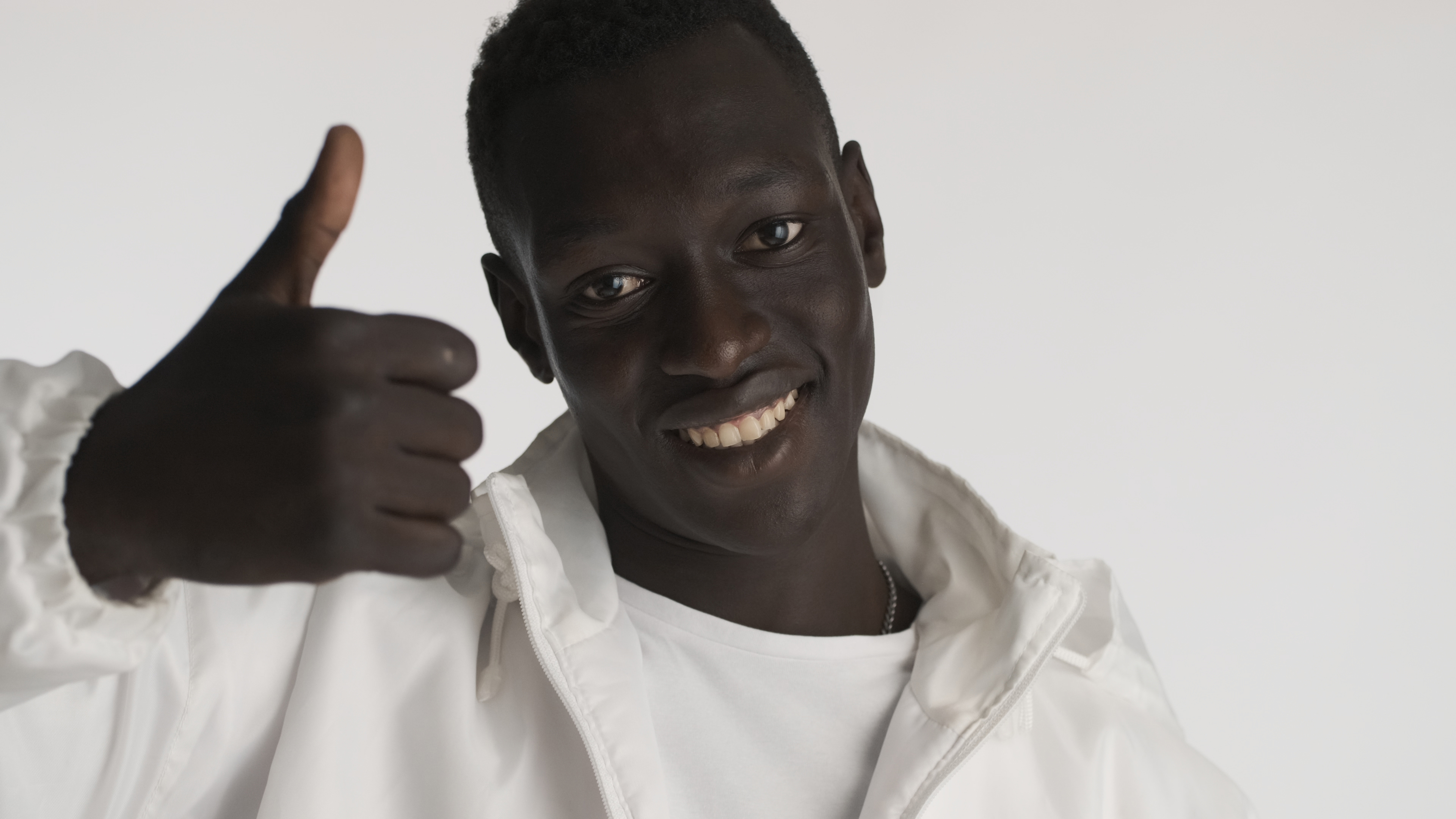 Attractive smiling African American man dressed in casual wear keeping thumb up looking happy over white background. Like it expression